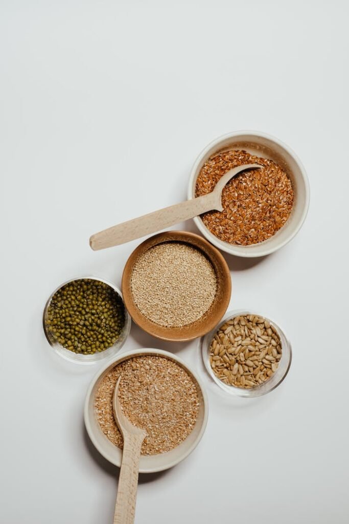 pexels-photo-7420515 Top view of assorted grains in bowls with wooden spoons on a minimalist background.